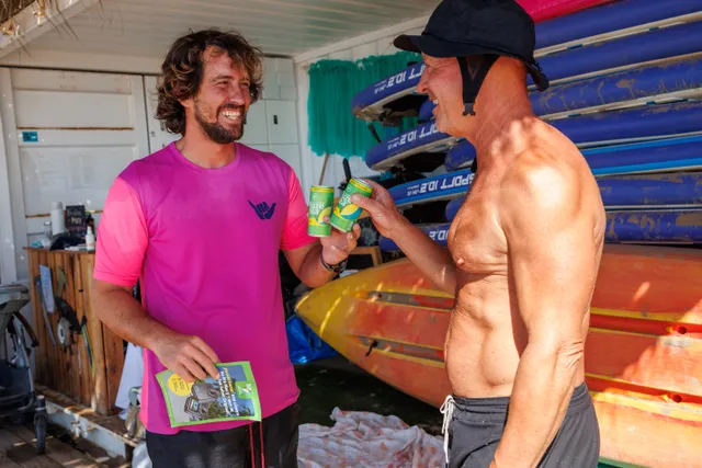 Dos personas brindando con latas de Fuze Tea en un chiringuito de surf