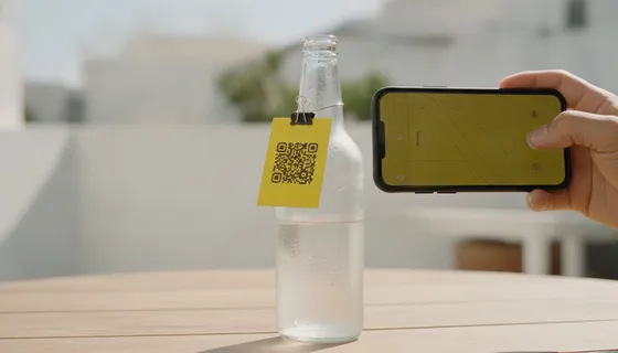 Mano escanea con el móvil el código QR de una tarjeta amarilla atada a una botella fría