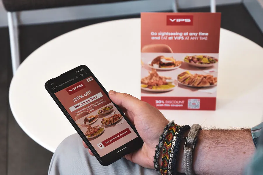 Móvil con la webapp de VIPS abierta junto al flyer del cupón de descuento